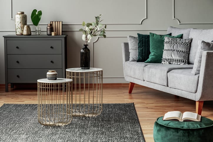Two stylish small coffee tables with marble tops in front of elegant grey couch with emerald pillows