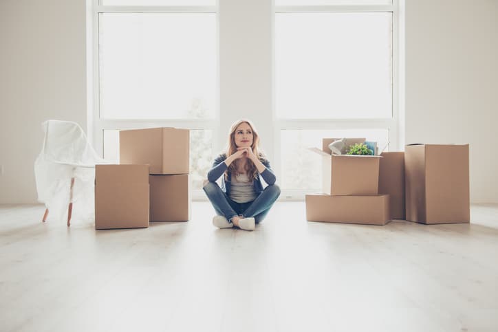 Dream come true! Portrait of young pretty woman sitting on the floor and thinking how to unpack all the stuff